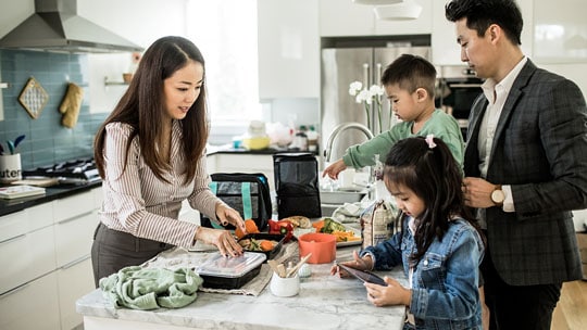 A family gathers in a kitchen as a woman prepares food.